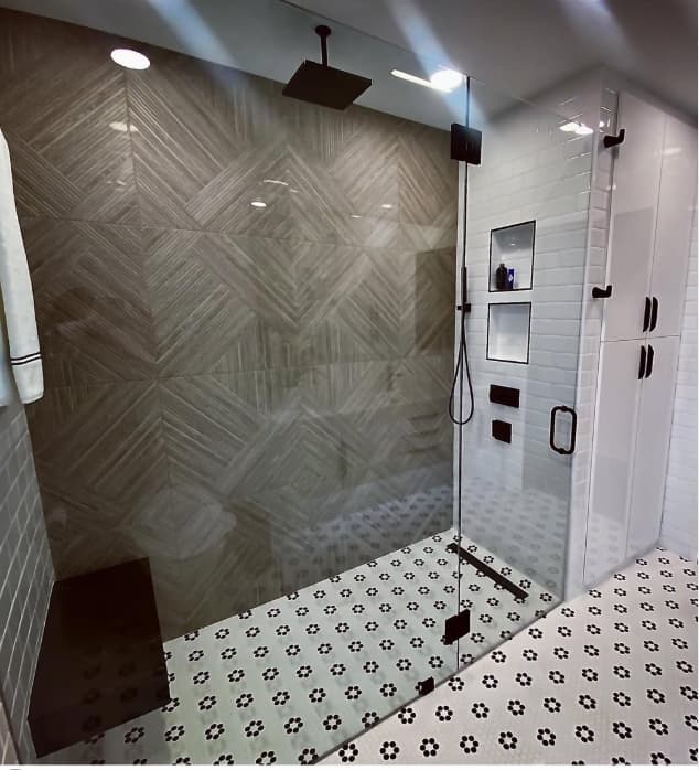 Walk-in glass shower with a stone herringbone feature wall, matte black fixtures, and floral mosaic flooring