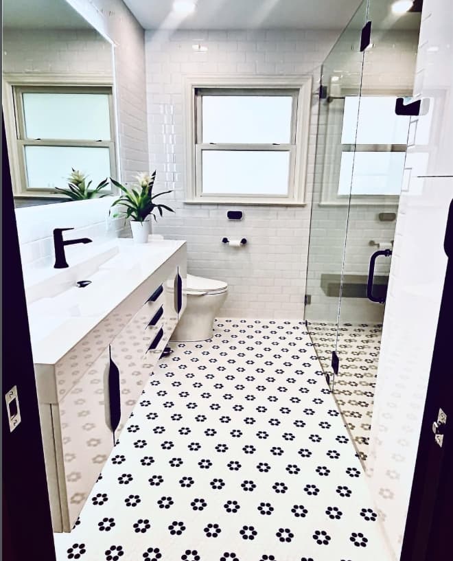 Bright white bathroom with a floating vanity, floral mosaic floor, frosted window, and glass shower