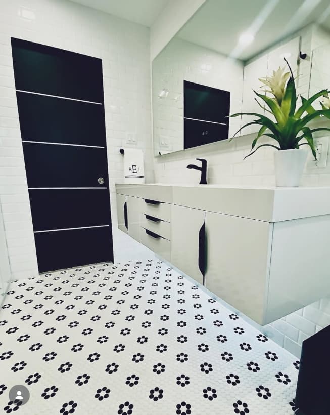 Modern white floating vanity with matte black fixtures, a black paneled door, and floral mosaic flooring