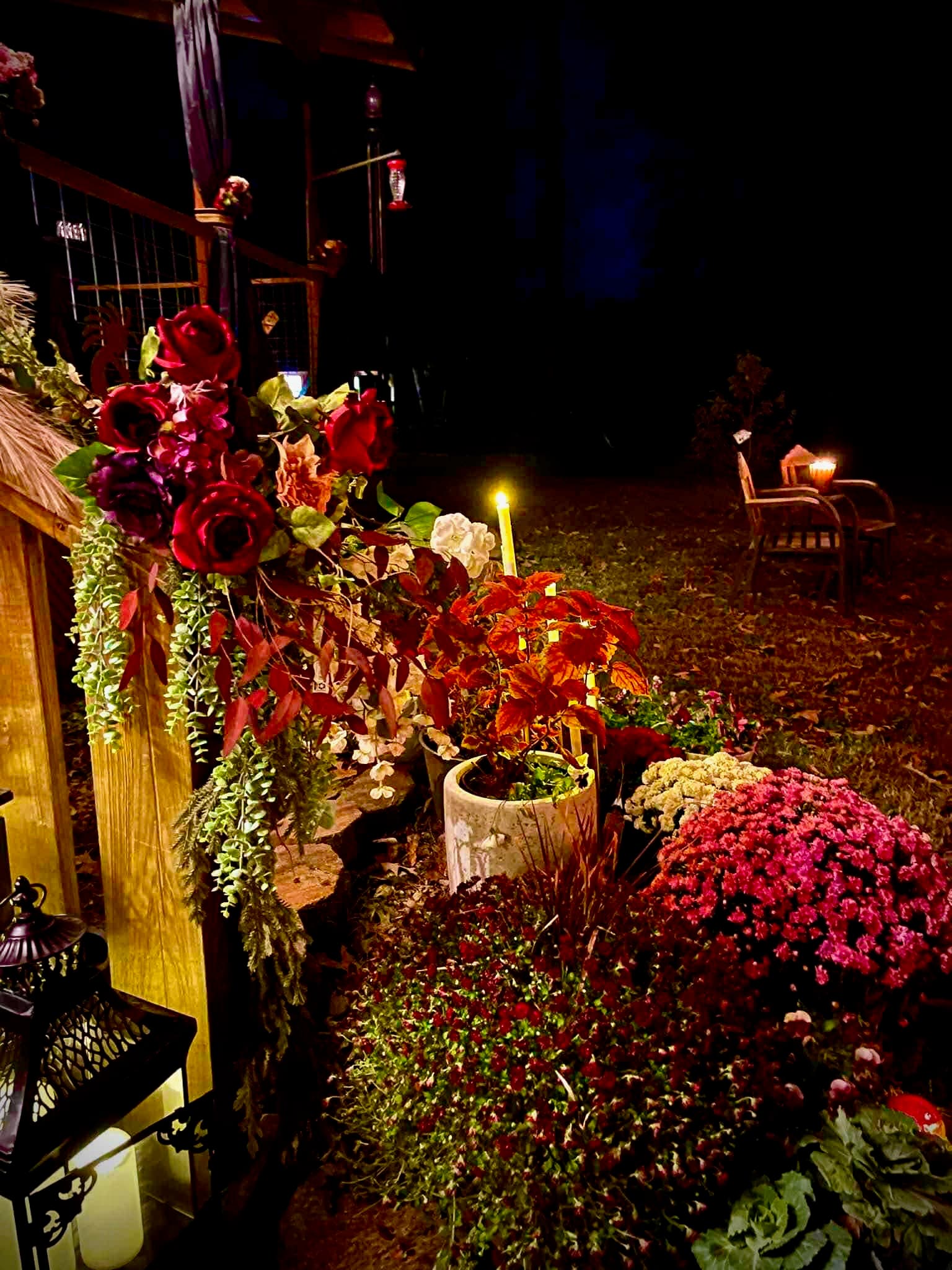 Candlelit autumn garden installation with burgundy roses, trailing greenery, and jewel-toned chrysanthemums