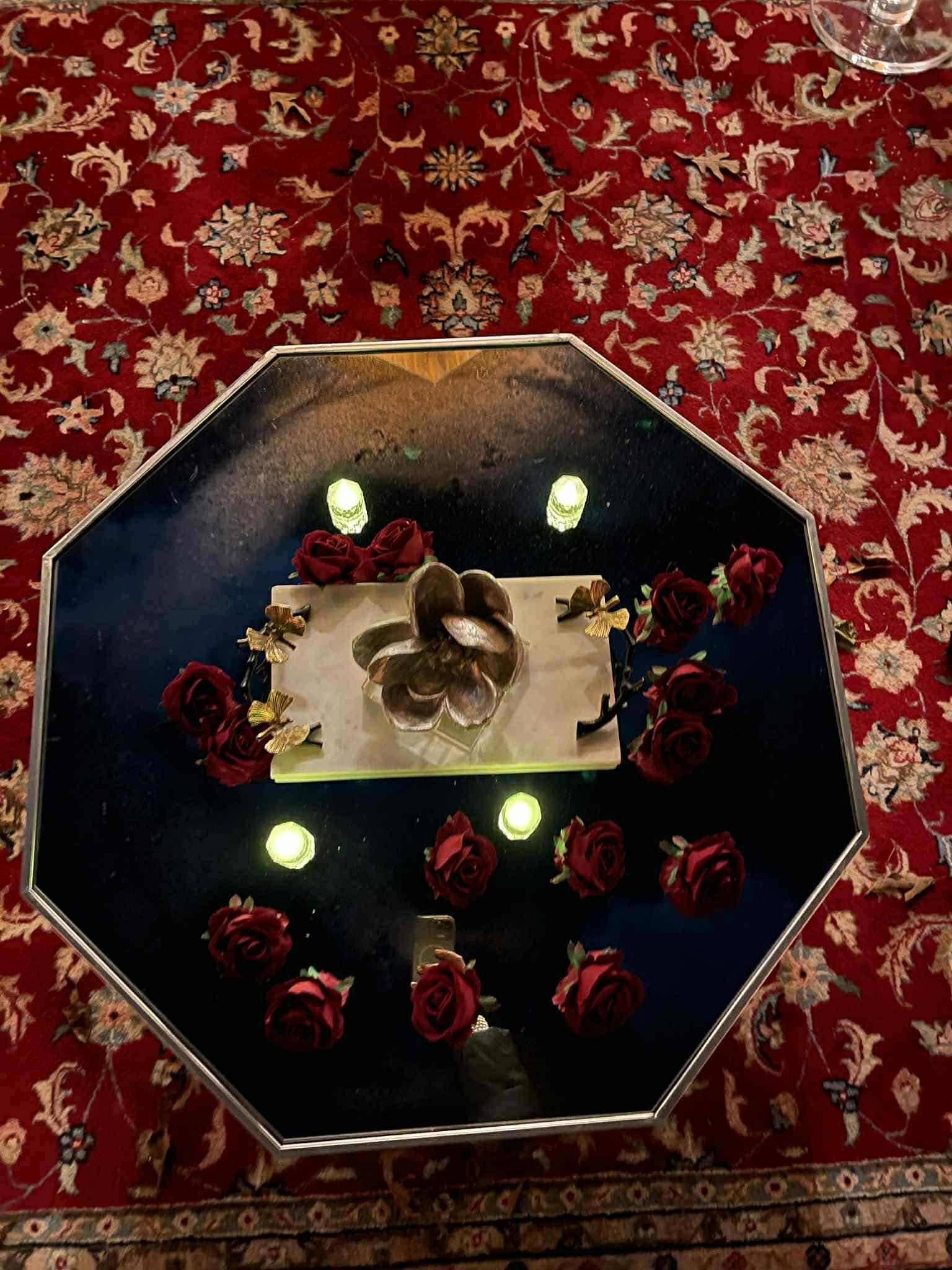 Octagonal mirrored table styled with deep red roses, gold botanical accents, and candlelight