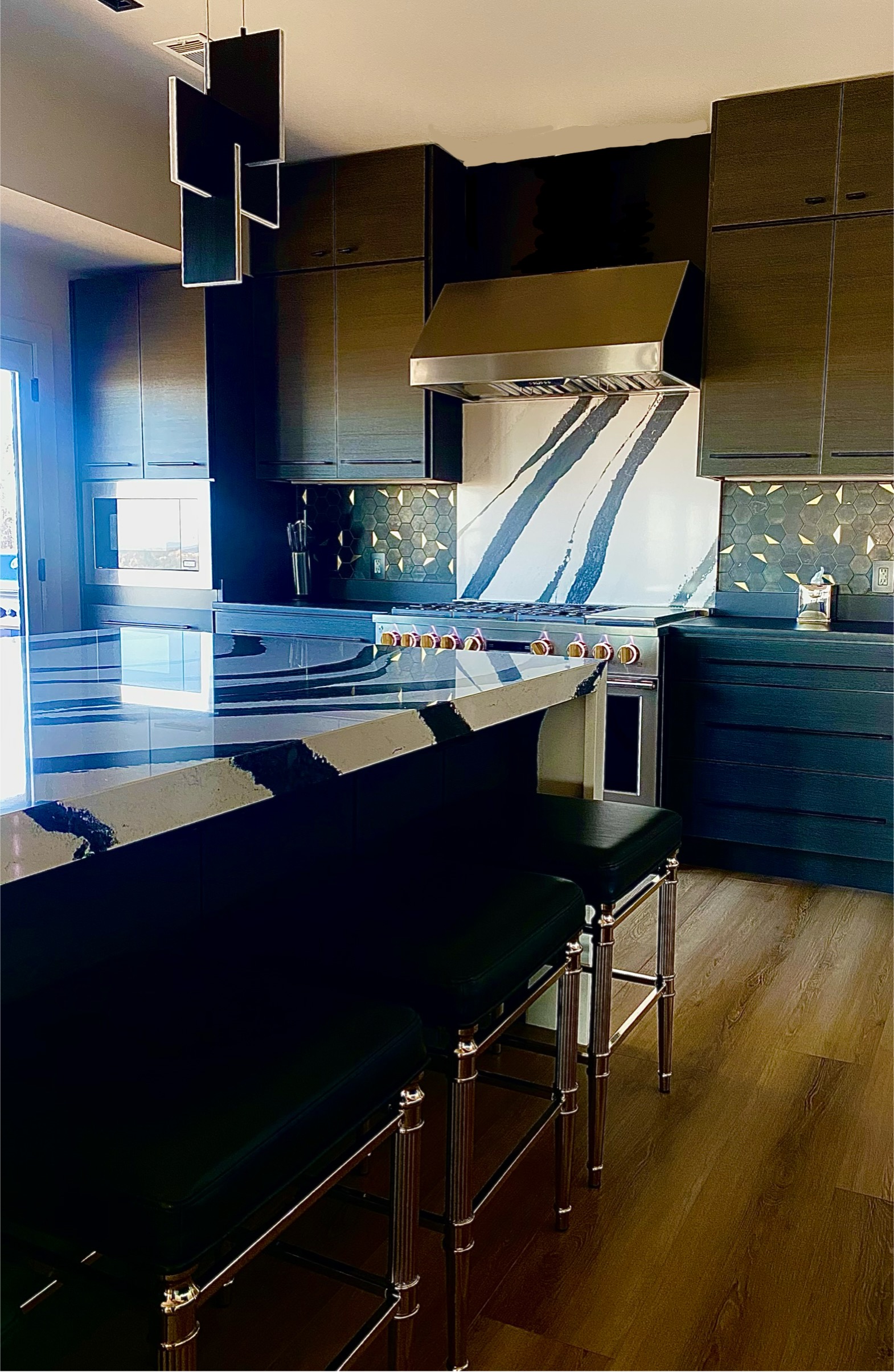 Luxury modern kitchen with dark wood cabinetry, dramatic black-and-white marble waterfall countertops, stainless steel range hood, and brass bar stools